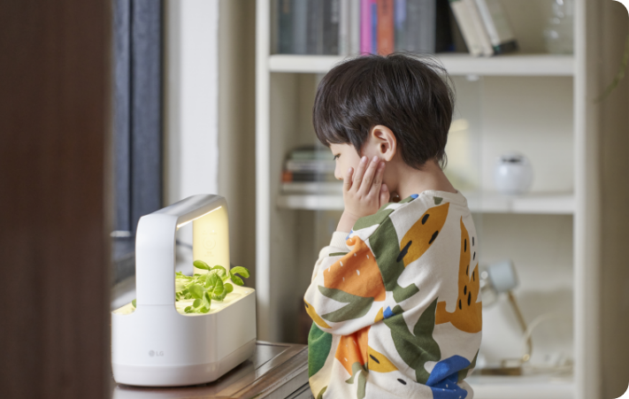 어린 아이가 LG 틔운 미니에 자라난 식물을 보고 신기해하는 모습