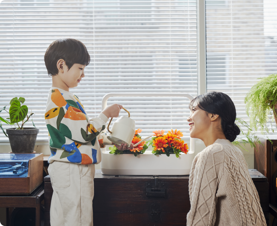 어린 아이와 어머니가 LG 틔운 미니에 자라난 식물에 함께 물을 주며 즐거워 하는 모습